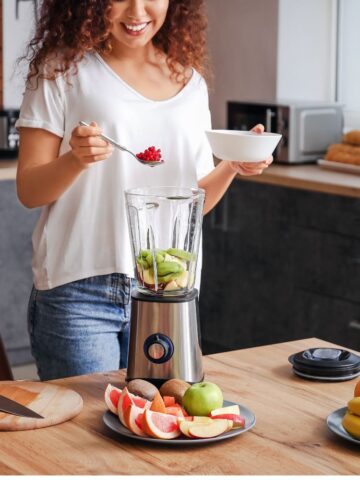 Woman putting berries in blender with fresh fruit