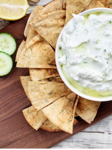 Bowl of dip surrounded by pita chips, lemon and cucumber