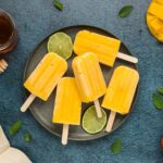 Mango popsicles on gray plate with cut limes and honey