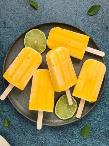 Mango popsicles on gray plate with cut limes and honey