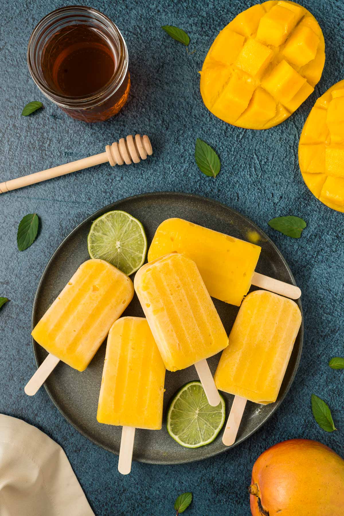 Mango popsicles on a gray plate with limes and cut mango