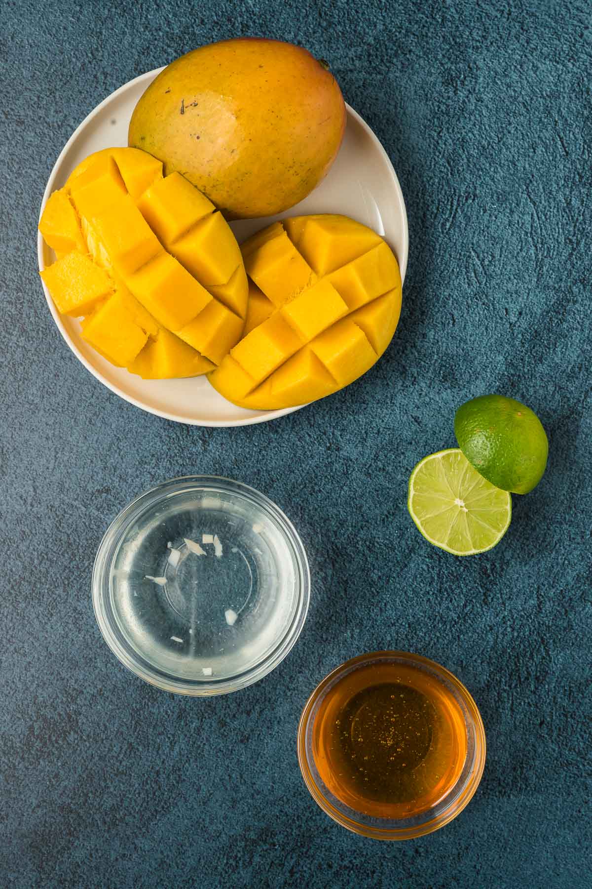 Mango popsicle ingredients including cut up mango, honey, coconut water and lime