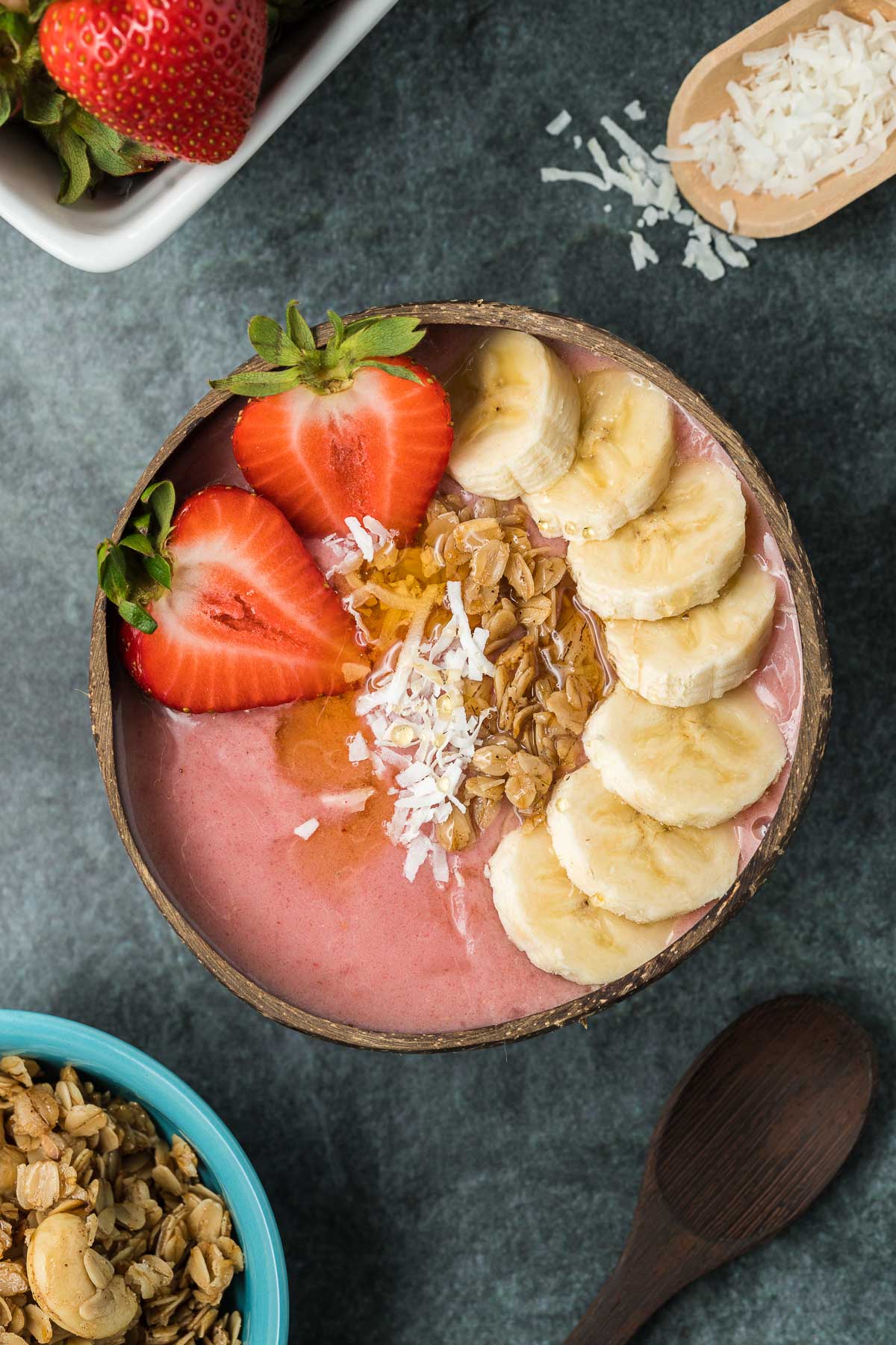 Strawberry banana smoothie bowl with bowl of granola and coconut flakes
