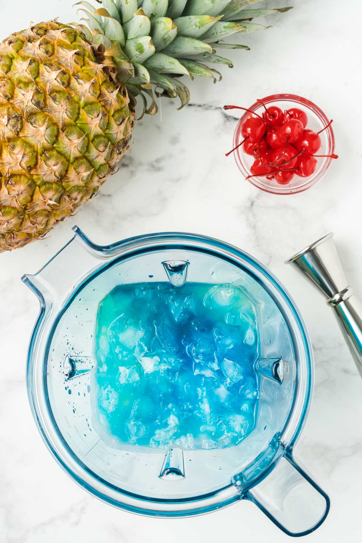 frozen blue hawaiian ingredients in a blender with pineapple and cherries in background